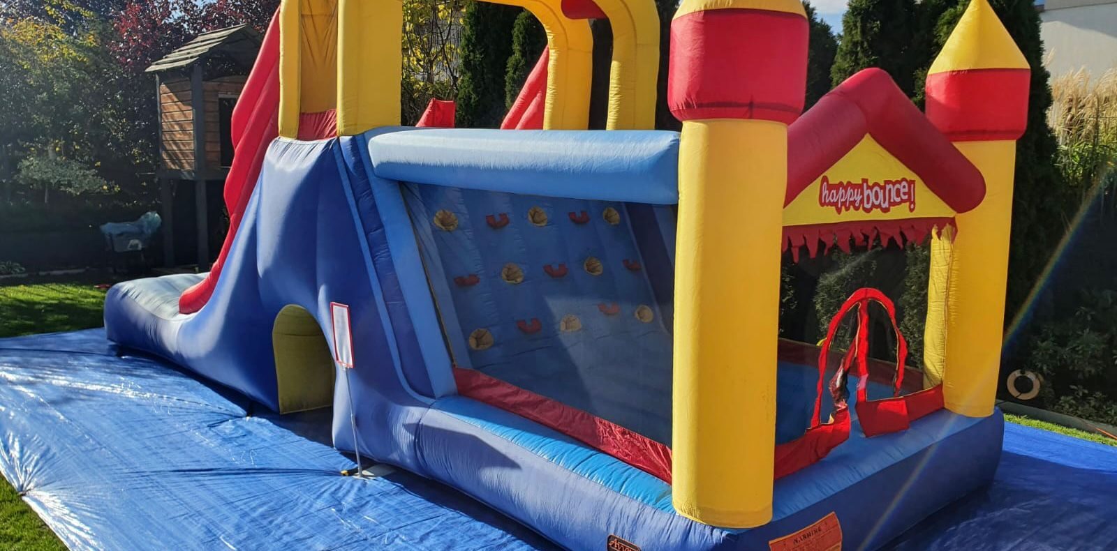 Bouncy castle – inflatable castle with slide and climbing wall on a tarpaulin in a garden